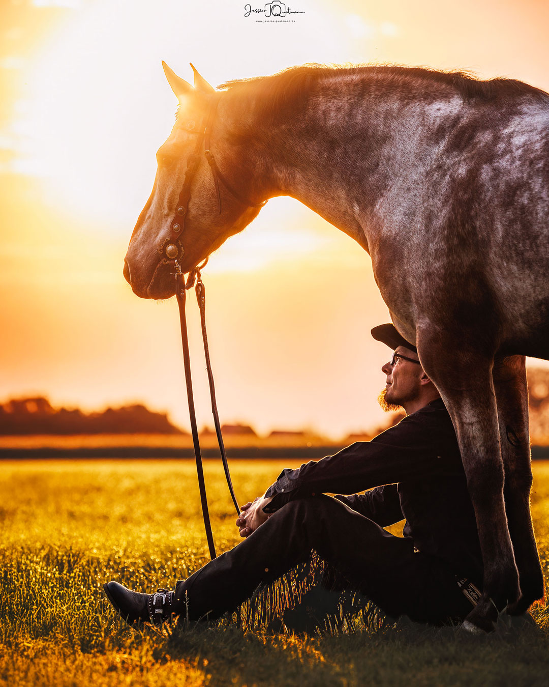 Sebastian Lampe sitzt auf den Boden vor seinem Pferd Pepe und sie schauen zusammen in den Sonnenuntergang.