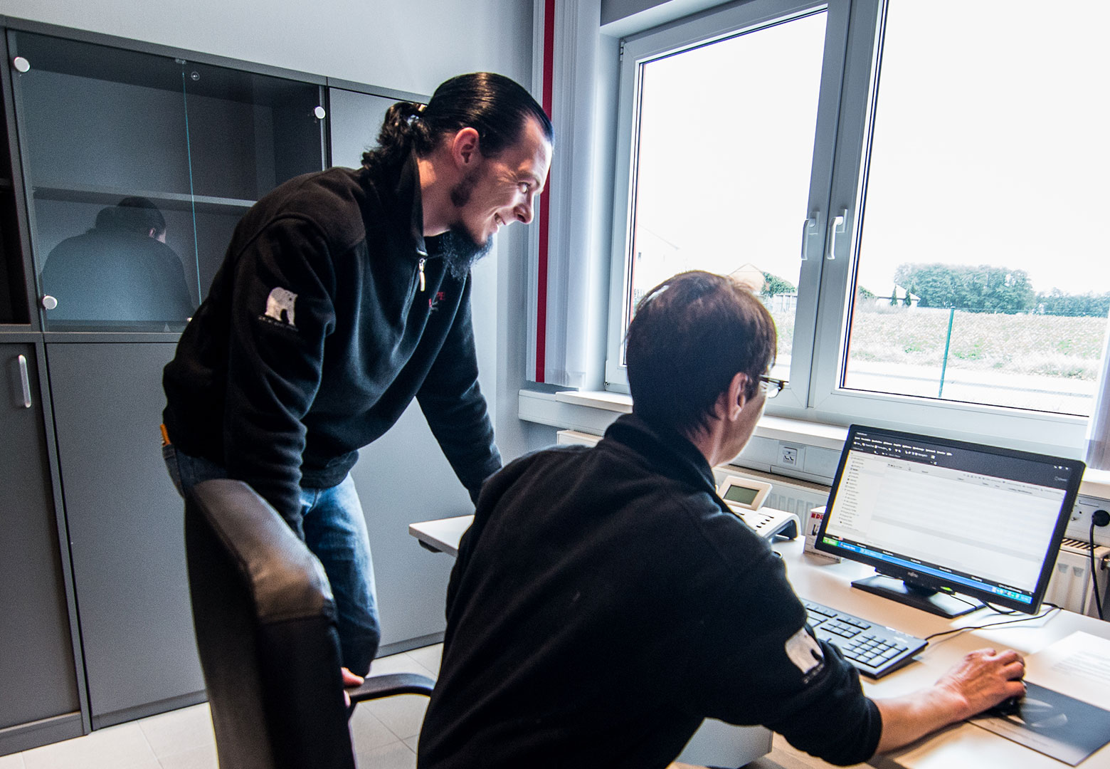 Der junge Sebastian Lampe steht neben Monika Lampe, die Ihm gerade etwas an dem PC zeigt.